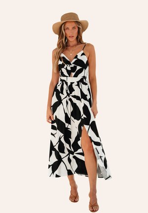 Maxi dress in black and white floral pattern, featuring a V-neck, spaghetti straps, high slit, and lightweight fabric. Worn with a straw hat.