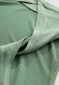 Grünes Stoffkleidungsstück mit glatter Textur, verfügt über ein V-Ausschnitt-Design und saubere Nähte entlang der Kanten.