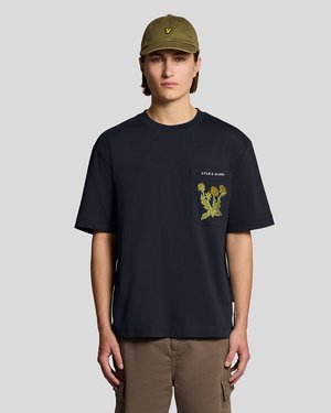 Junger Mann trägt eine olivgrüne Mütze und ein schwarzes T-Shirt mit gelbem Löwenzahn-Design und dem Text "LYLE & SCOTT" auf der Brusttasche.