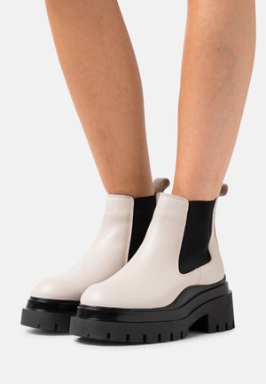 Bottes Chelsea en cuir beige avec des côtés élastiques noirs, bout rond et semelle plateforme noire épaisse avec un motif texturé.