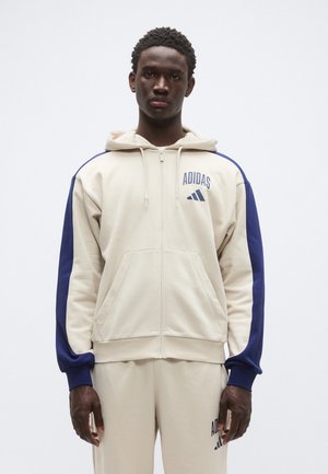 Bézs zipzáras kapucnis pulóver tengerészkék ujjakkal és kapucnival. Az "Adidas" logója a mellkason, csíkok az ujjakon. Simább tapintású anyag.