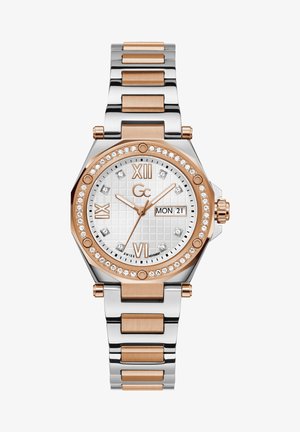 Hõbeda ja roosa kuldne metallkell oktagonaalse korpusega, valge tekstureeritud kellaseier, Rooma numbrid ja kristallid kroonpinna ümber, kuupäeva kuvamine.