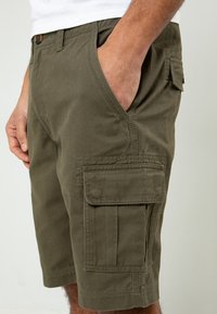 Shorts cargo en vert olive, fabriqués en tissu durable, avec des poches latérales, une poche avant avec un bouton et une coupe décontractée.