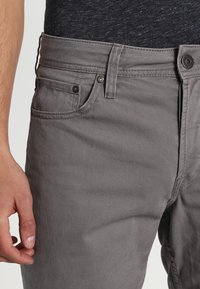 Šedé bavlněné plátěné kalhoty s klasickým pětipocket designem, se železnými knoflíky a viditelným šitím. Hladká textura a přiléhavý střih.
