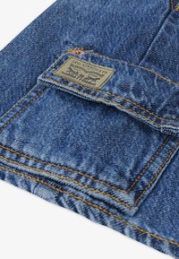 Μπλε τζιν ύφασμα με ένα πατς που φέρει το λογότυπο «Levi Strauss & Co.» και αντίθετη κίτρινη ραφή κατά μήκος των άκρων και της τσέπης.