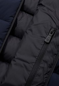 Zwart gewatteerd jackinterieur met een gladde stof, gestikte secties en een zichtbare rits met een ronde trekker.