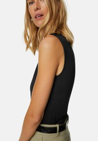 Svart ärmlös bodysuit med en figurnära design, slät yta och rund halsringning, parat med högmidjade ljusa byxor och ett svart bälte.