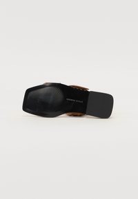 Sandale en cuir marron avec une semelle en caoutchouc noir, présentant un motif texturé. Le design inclut une large sangle sur le pied.