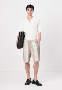 Leichtes, kurzärmliges weißes Hemd; beige und weiße gestreifte Shorts mit Kordelzug; schwarze Tragetasche; schwarze Schuhe.