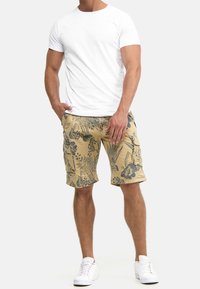 T-shirt blanc à col rond associé à un short cargo beige avec des motifs floraux sombres. Modèle portant des baskets de sport blanches.