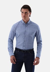 Helles blaues Kurzarmhemd mit Karomuster, mit Kragen und langen Ärmeln, kombiniert mit dunklen Jeans und einem schwarzen Gürtel.