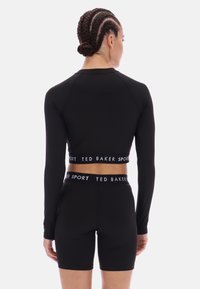 Juodas sportinis trumpas topas su ilgomis rankovėmis ir kontrastinga juosta, kurioje užrašas "TED BAKER SPORT“. Derinamas su atitinkamais juodais šortais.