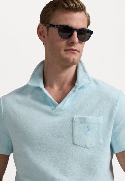 Lichtblauw terry polo shirt met een klein zakje en een kraag met twee knopen. Gemaakt met donkere ronde zonnebrillen. Gecontroleerde stof.
