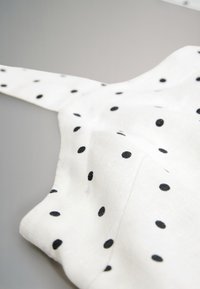 White fabric with black polka dots, featuring a soft texture and a smooth finish, includes a thin strap and is slightly wrinkled.