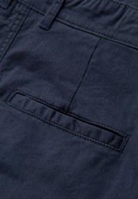 Gros plan sur un tissu bleu marine avec une poche passepoilée horizontale et des coutures visibles sur un vêtement.