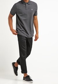 Ciemnoszara koszulka polo z krótkimi rękawami i zapinanym kołnierzykiem, zestawiona z czarnymi spodniami i czarnymi trampkami z białymi podeszwami.