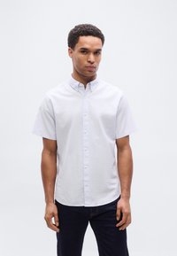 Ανοιχτό μπλε κοντομάνικο πουκάμισο με κουμπιά, κατασκευασμένο από υλικό βαμβακερού μείγματος. Διαθέτει κλασικό γιακά και διακριτή υφή· φοριέται με σκούρο τζιν.