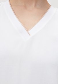 Top bianco a scollo a V con una texture liscia, caratterizzato da un bordo di un beige chiaro in contrasto lungo il collo.