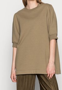 Khaki oversized pulovrová košile s krátkými nabíranými rukávy, kulatým výstřihem a rovým lemem. Hladká bavlněná textura.