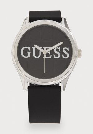 Black rubber watch with a silver-tone metal case, round face, and bold "GUESS" logo. Features a textured dark dial and silver hands.