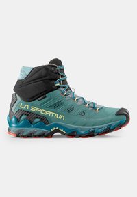 Scarpa da trekking alta in teal e nero, con pannelli testurizzati, colletto flessibile e suola robusta con accenti rossi.