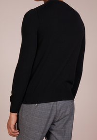 Musta neulottu villapaita, jossa on pyöreä pääntie ja resorit hihansuissa, yhdistetty harmaisiin ruutuhousuihin, joissa on nappikoristelu.