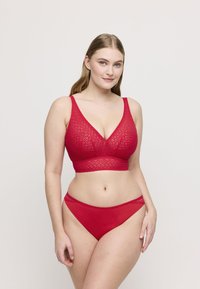 Punainen pitsinen bralette, jossa on V-pääntie, leveät hihnat ja saumaton muotoilu. Samasta punaisesta pitsistä valmistetut bikinit, joissa on herkät aaltoilevat reunat.