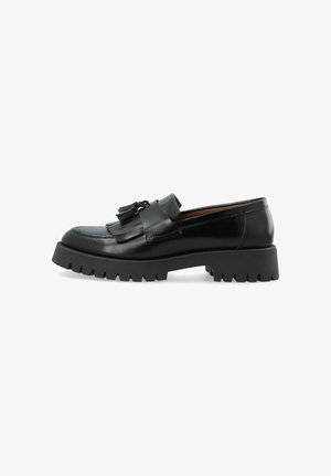 Mocassin en cuir noir avec une semelle épaisse à crampons, des glands décoratifs et des franges sur le dessus, vu de profil sur fond blanc.