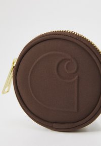 Runder brauner Stoffbeutel mit strukturiertem Logo, ausgestattet mit einem goldenen Reißverschluss und Zugriegel. Glatte Außenseite mit sichtbaren Nähdetails.