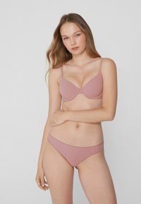 Lichtroze beha en bijpassende bikini slip, met een gladde stof, verstelbare banden en subtiele stikselaccenten. Eenvoudig ontwerp en pasvorm.