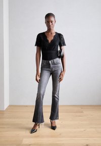 Body en dentelle noire avec un décolleté en V profond et des manches courtes, associé à un jean grisé évasé avec un ourlet effiloché et des escarpins noirs.