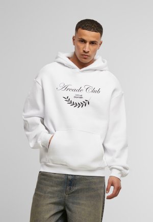 Sudadera blanca con un bolsillo frontal tipo canguro y texto negro que dice "Arcade Club" con un diseño de hoja, combinada con jeans de lavado claro.