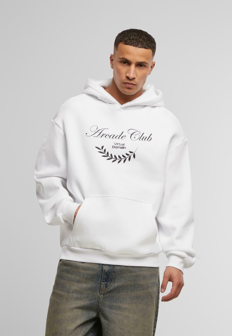 Felpa bianca con cappuccio, dotata di tasca a marsupio frontale e testo nero che dice "Arcade Club" con un design a forma di foglia, abbinata a jeans chiari.
