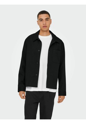 Black button-up shirt with a collar, long sleeves, and a single chest pocket, worn over a white t-shirt. Smooth fabric and relaxed fit.