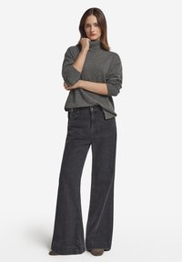 Grauer Rollkragenpullover mit lockerem Schnitt, kombiniert mit hoch-taillierten, weit geschnittenen schwarzen Denim-Jeans. Glatte Textur und dezente Rippenstrickdetails.