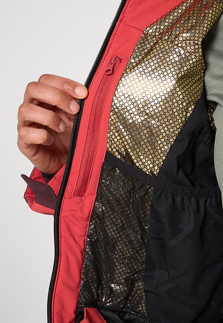 Rote Jacke mit einem Reißverschluss, die eine glänzende goldene Netzfutter und schwarze Stoff darunter zeigt. Strukturiertes Material schafft ein geschichtetes Erscheinungsbild.