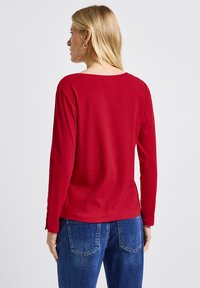 Röd ribbad långärmad topp med bred halsringning, med rakskurna ärmar och avslappnad passform, matchad med blå jeans.