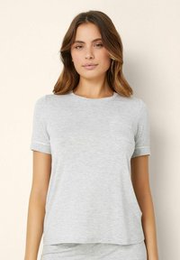 Tricou scurt, gri, dintr-un material moale și ușor. Are un decolteu rotund și un mic buzunar pe piept, cu manșete ale mânecilor rulate.