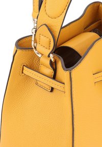 Sac à main en cuir jaune avec une finition texturée, doté d'un garniture foncée et d'une forme structurée. Comprend une bandoulière amovible et une quincaillerie argentée brillante.