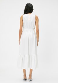 Robe midi blanche avec un tissu texturé, une taille ceinturée et un ourlet à volants à plusieurs niveaux. Présente un dos en clé et un design sans manches.