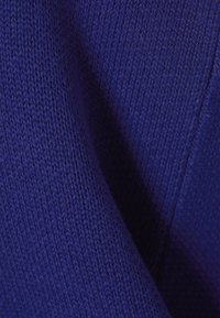 Primo piano di un tessuto lavorato a maglia di un blu scuro texture, con punti visibili e pieghe che creano ombre e profondità.