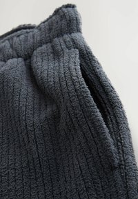 Tissu gris texturé avec un design à cannelures, présentant une surface douce et duveteuse. Le vêtement a une coupe décontractée et une taille élastique.