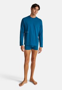 Langue mouwen turkooise shirt met ronde halslijn en bijpassende boxershorts. De stof lijkt glad; het shirt heeft minimale tekstdetails.