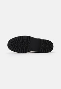 Suela de zapato negra con surcos profundos y robustos diseñados para proporcionar agarre, mostrada sobre un fondo blanco liso.