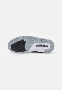 Semelle de chaussure avec une bande de roulement en caoutchouc gris, noir et blanc présentant des motifs circulaires et le logo "JORDAN" en noir et blanc.