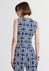 Top senza maniche di colore blu navy con motivo geometrico bianco. Design aderente con una texture liscia, con scollo rotondo e dettagli sulla schiena.