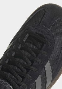 Svart mocka och mesh sneakers med grå ränder, featuring platta svarta snören och strukturerad gummisula för grepp. Nära vy.