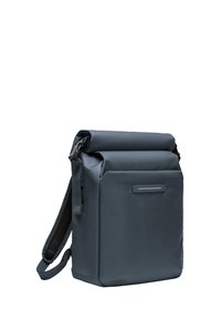 Sac à dos à rabat gris foncé en tissu imperméable, avec une poche avant, une sangle d'épaule réglable et une surface texturée.