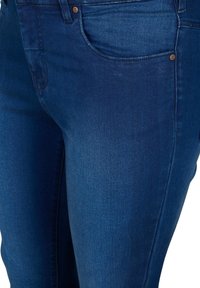 Vaqueros de mezclilla azul oscuro con una vista en primer plano del bolsillo delantero, que presenta un remache de cobre y una textura suave con ligeros desvanecimientos.