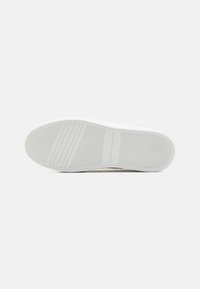 White rubber outsole with thin horizontal and vertical grooves for traction, featuring a subtle embossed logo detail. Smooth surface texture.